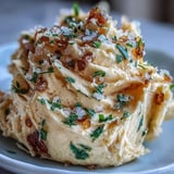 A creamy spread of salted honey butter melting on warm, crusty bread with visible herb flecks and golden honey swirls.