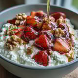 Fresh cottage cheese fruit bowl with strawberries and honey, a colorful and creamy breakfast delight topped with crunchy nuts and juicy berries.