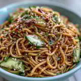 A vibrant, chilled sesame noodle dish with crunchy cucumber, carrots, and a drizzle of nutty sesame sauce for a refreshing meal.