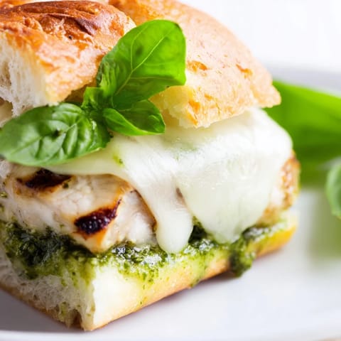 Pesto Chicken Melt served on a plate with fresh basil leaves and ripe tomato slices, ready to be enjoyed.