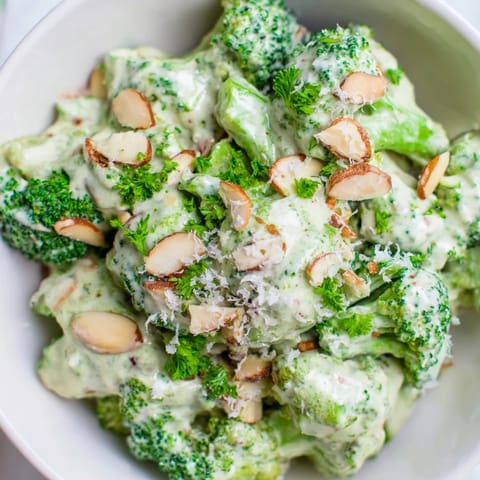 Freshly tossed Garlic Parmesan Broccoli Salad on a wooden table, garnished with chopped parsley and extra grated Parmesan for a quick, gluten-free side.