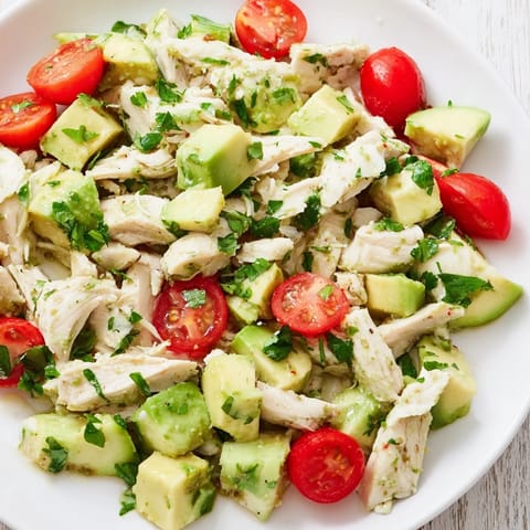 A close-up of creamy avocado chicken salad with herbs, red onion, and cucumber, served on a rustic wooden table.  