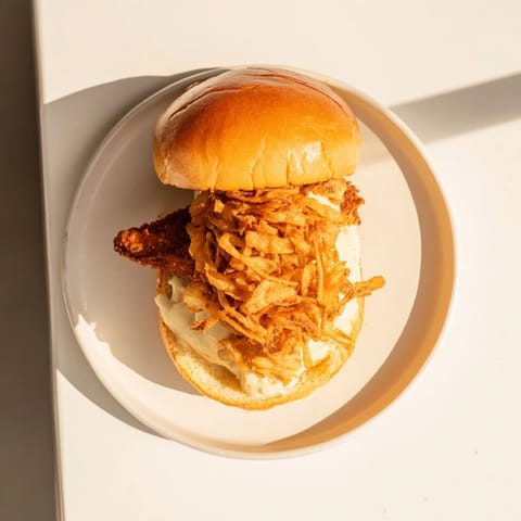 A close-up of a Crispy Onion Chicken Sandwich layered with lettuce and golden fried onions.  
