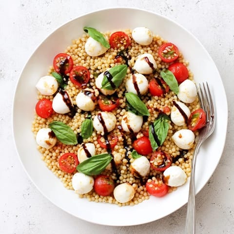 A vibrant Caprese Couscous Salad served in a shallow bowl, featuring tender Israeli couscous, juicy tomatoes, creamy mozzarella, and fresh basil.  