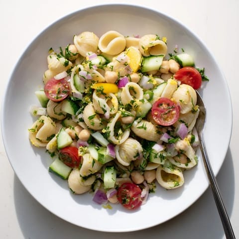 A close-up of a vibrant Lemon Herb Chickpea Pasta Salad garnished with crumbled feta, kalamata olives, and fresh mint.