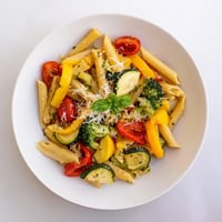 Colorful roasted vegetables and penne pasta tossed with garlic olive oil and fresh basil, topped with grated Parmesan and lemon wedges.